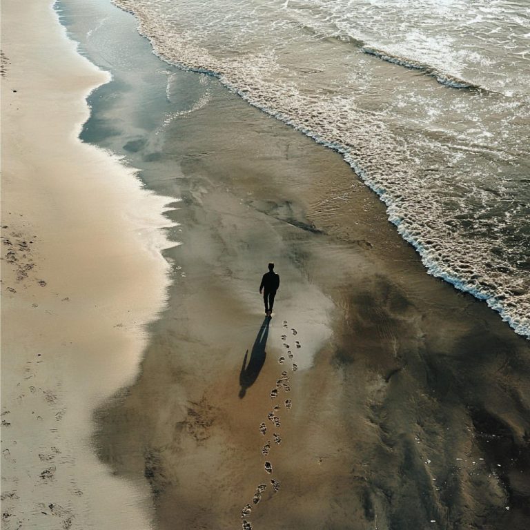 A person walking alone on a sandy beach, with waves lapping at the shore.