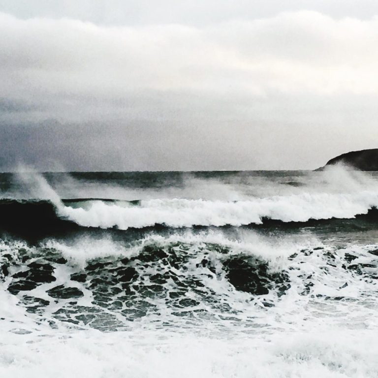 Rough sea waves crashing against a rocky shore under a cloudy sky.